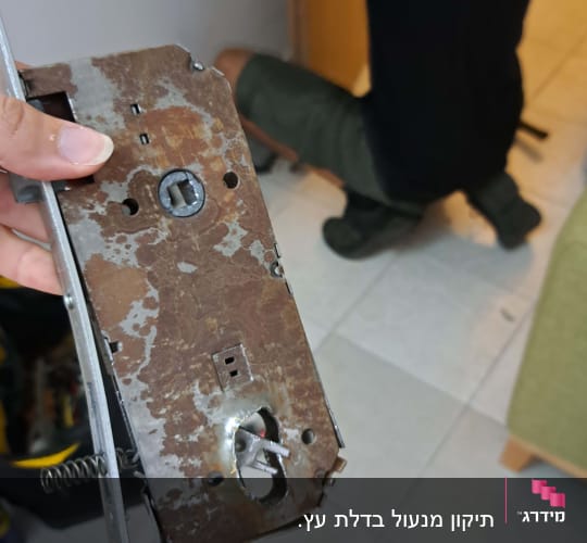 מנעול חלוד מוחזק ביד, אדם עובד על דלת